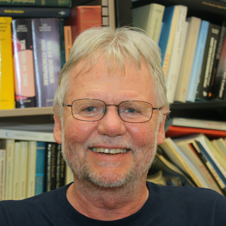 Dr. George Fisher smiling in front of a bookcase