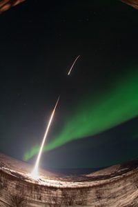 Night sky with green cloud like form in sky, rocket launch into sky from ground.