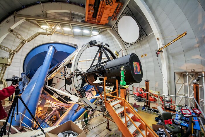 Inside a large white rounded room, a black round tube (DESI) is attached to a larger structure. A set of orange stairs leads to DESI.