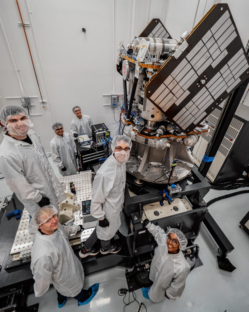 Men and women in bunny suits around spacecraft.