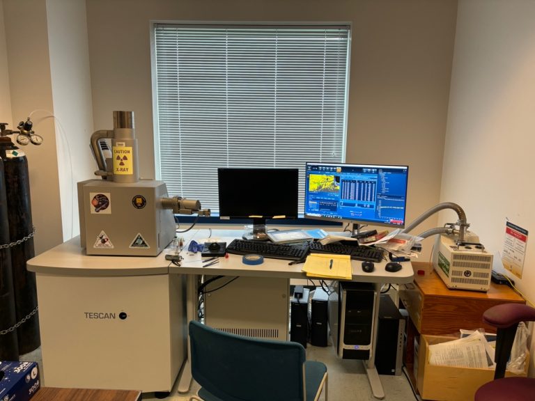 the SEM instrument, on a desk next to two computer monitors